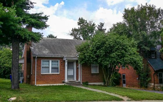 Charming brick suburban home with lush greenery and inviting front entrance, perfect for cozy living.