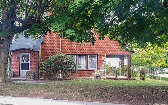 Charming brick house with lush greenery, nestled in a serene neighborhood under the shade of beautiful trees.