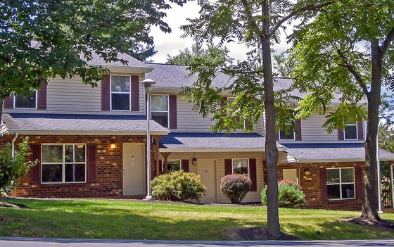 Charming townhouse with brick facade and lush greenery, nestled in a serene, tree-lined neighborhood.