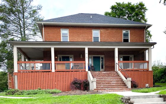 Charming brick duplex with spacious front porch, classic design, and beautiful greenery in a serene neighborhood setting.