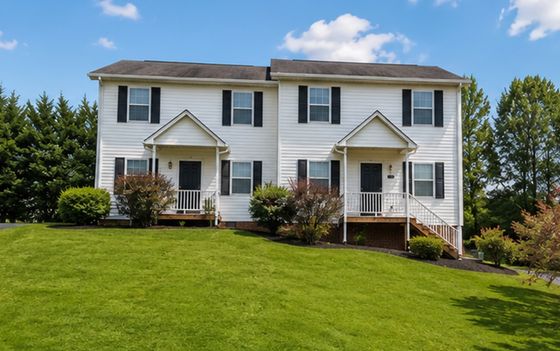 Charming duplex with crisp white facade, black shutters, and welcoming porches set on a lush green lawn.