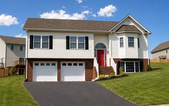 Charming split-level home with a red front door, dual garages, and lush green lawn under a bright blue sky.