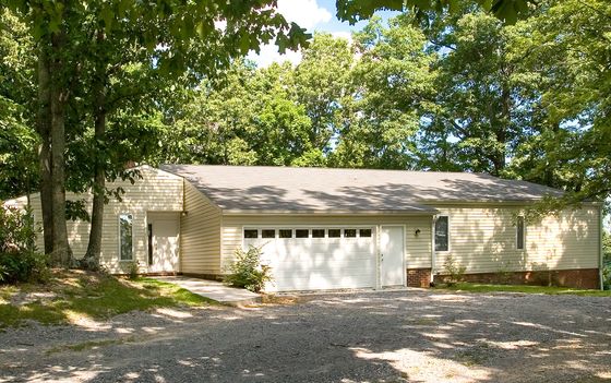 Charming single-story home with a spacious driveway, nestled among lush trees, offering serene and private living.