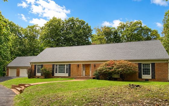 Charming brick home with inviting front porch, nestled in lush greenery under a bright blue sky.