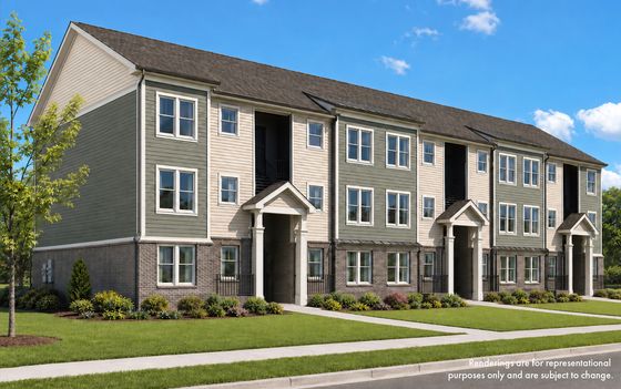 Elegant three-story apartment building with classic architecture, lush green landscaping, and inviting entrances under a clear blue sky.