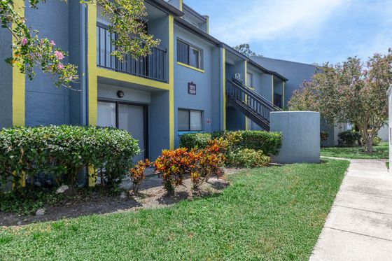 Charming apartment exterior with vibrant landscaping and modern blue facade under a sunny sky.