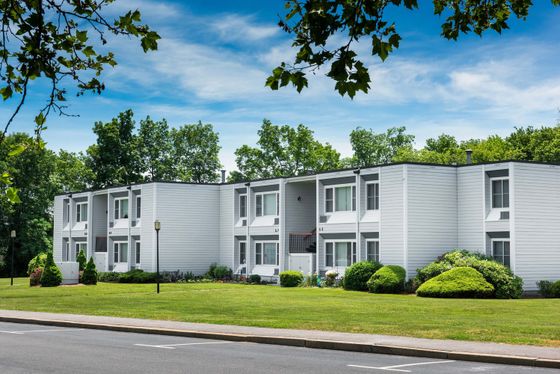 Charming white apartment complex surrounded by lush greenery and a vibrant lawn, perfect for serene living.