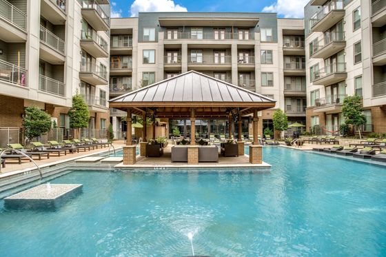 Luxurious apartment complex with modern architecture featuring a sparkling pool, shaded lounge area, and well-designed landscaping.