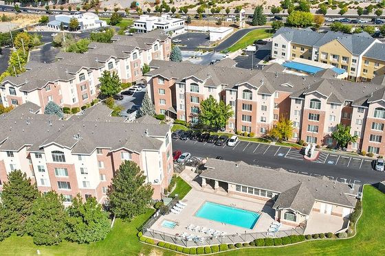 Aerial view of a modern apartment complex featuring beautifully landscaped surroundings, a pristine swimming pool, and ample parking in a vibrant urban setting.