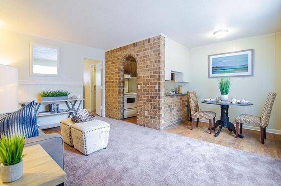Charming open-concept living space with cozy seating area, stylish dining nook, and a rustic brick kitchen accent wall, perfect for modern living.