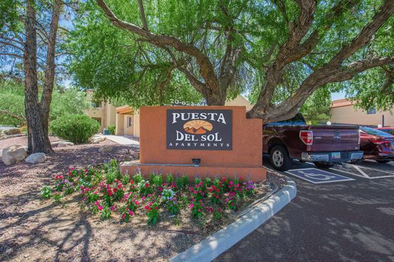 Charming Puesta Del Sol Apartments entrance sign surrounded by lush greenery and vibrant flowers, offering a welcoming and serene environment.