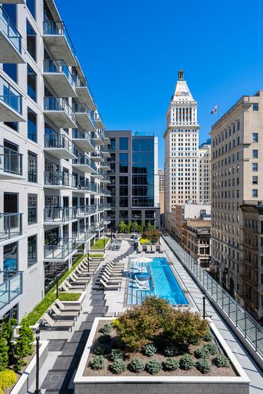 Luxurious cityscape view with modern apartments, spacious rooftop terrace, and sparkling pool amid urban skyline.