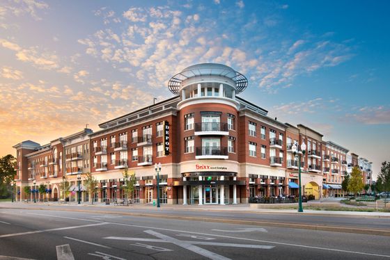 Elegant urban apartment complex with modern architecture and vibrant street-level shops, bathed in beautiful sunset light.