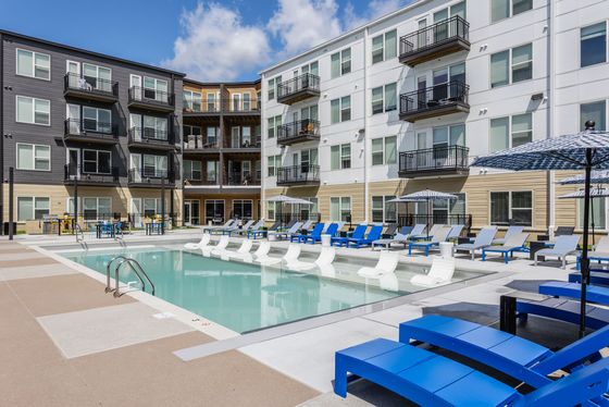 Modern apartment complex with a luxurious pool area, vibrant blue loungers, and stylish umbrellas, perfect for relaxation and socializing.