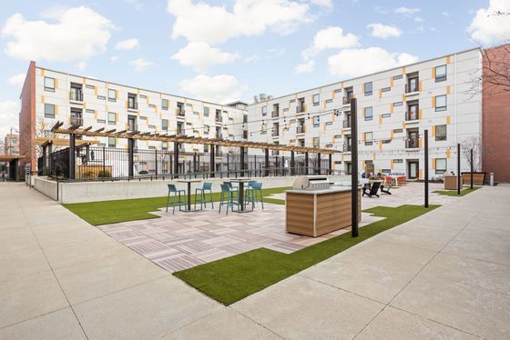 Modern apartment courtyard featuring stylish seating, barbecue grill, and lush greenery under a bright blue sky.