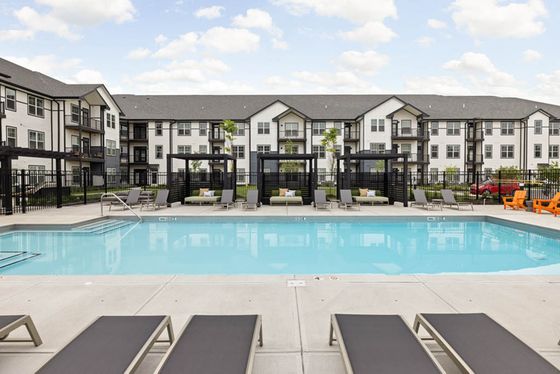 Inviting outdoor pool area with sleek loungers and modern apartment complex in the background, perfect for relaxation and leisure.