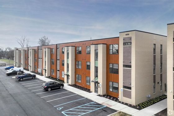 Modern apartment building exterior with sleek design, ample parking, and natural surroundings, offering a blend of urban and serene living.