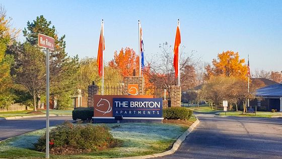 Charming entrance to The Brixton Apartments adorned with vibrant autumn foliage and sleek flags, offering a welcoming atmosphere in a serene setting.