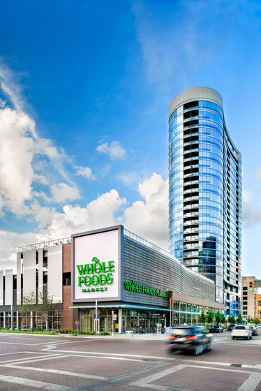 Modern high-rise apartment building with sleek glass facade above a Whole Foods Market, perfectly located for convenience and style.