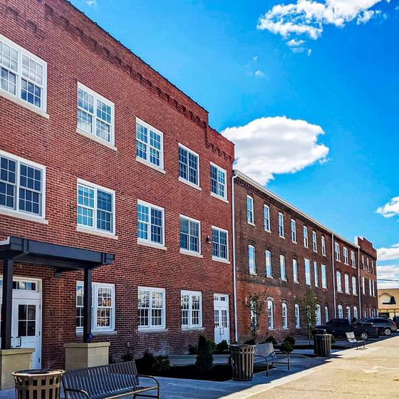 Charming brick apartment building with large windows, set against a vibrant blue sky, offering modern living in a historic setting.