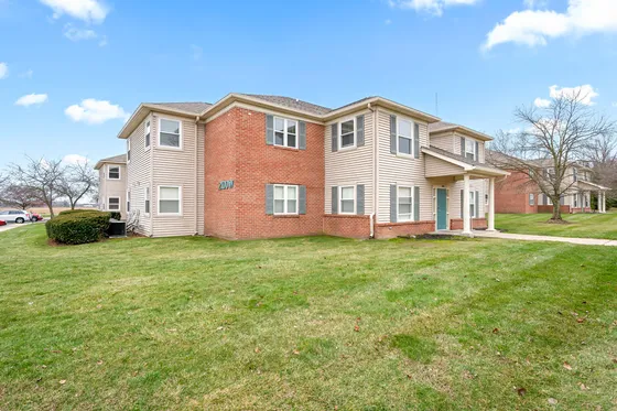 Charming two-story brick and siding apartment building surrounded by lush green lawns and a clear blue sky, offering a serene residential setting.