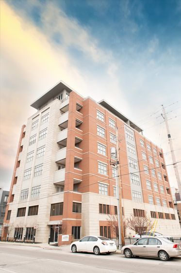 Modern urban apartment building with a sleek design, featuring brick and light-colored walls against a vibrant sky backdrop.