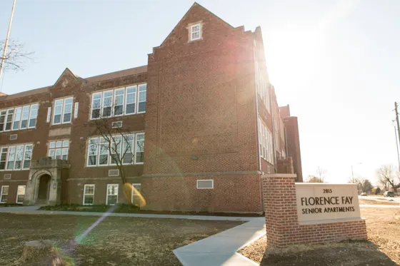 Elegant brick building with large windows, showcasing the Florence Fay Senior Apartments with a welcoming entrance bathed in warm sunlight.