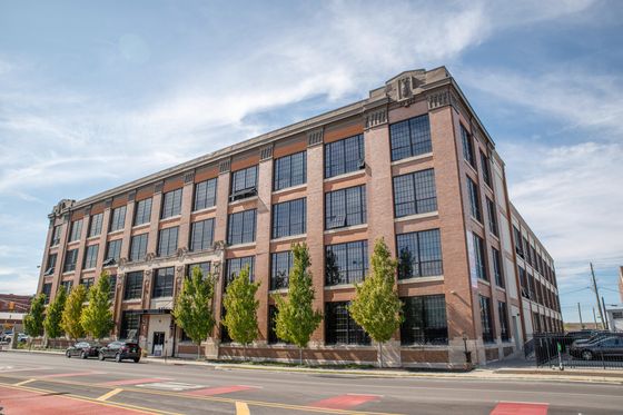 Charming urban loft building with historic brick facade and large industrial-style windows under a bright blue sky.