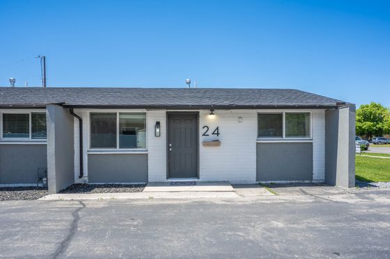 Charming single-story unit with modern gray accents and large windows, set against a bright blue sky, perfect for cozy living.