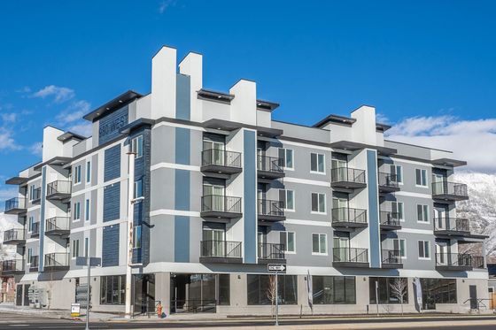 Modern four-story apartment building with sleek balconies and a stunning mountain backdrop under a clear blue sky.