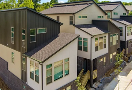 Modern townhouse complex with unique architectural design, featuring large windows and sloped roofs surrounded by lush greenery.