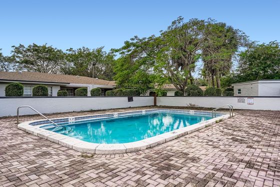 Inviting outdoor pool area with crystal-clear water, surrounded by lush greenery and elegant brick paving.