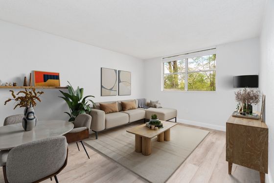 Chic living room with modern decor, featuring a large beige sectional sofa, stylish wooden coffee table, and abundant natural light from a large window overlooking greenery.