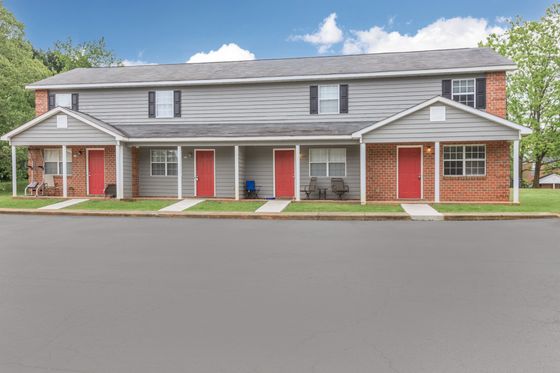 Charming townhouse exterior with inviting red doors and cozy front porches, surrounded by lush greenery.
