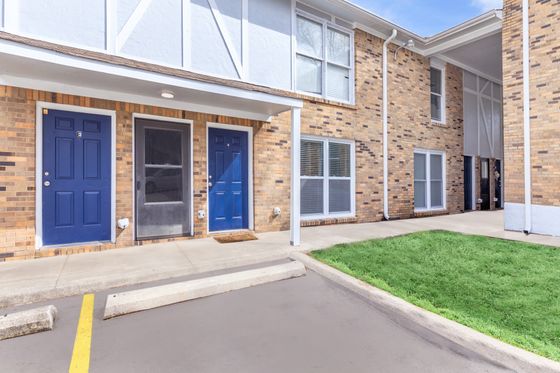Charming apartment exterior with modern blue doors, inviting walkway, and vibrant green lawn, perfect for comfortable urban living.