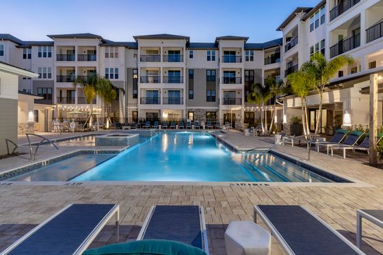 Luxurious apartment complex with a sparkling swimming pool, stylish poolside loungers, and elegant outdoor lighting creating a perfect evening ambiance.