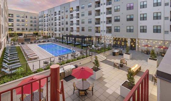 Luxurious apartment courtyard featuring a sparkling swimming pool, elegant lounge chairs, and ambient lighting for evening relaxation.