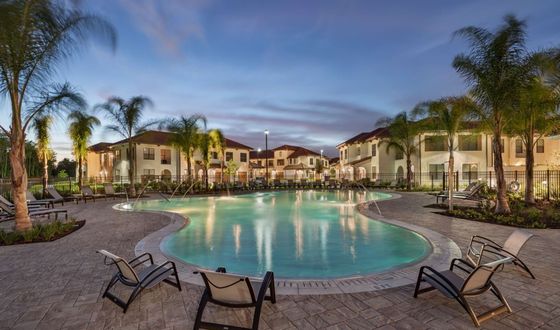 Luxurious apartment complex with a stunning resort-style pool surrounded by elegant palm trees and modern lounge chairs, highlighting a tranquil evening ambiance.