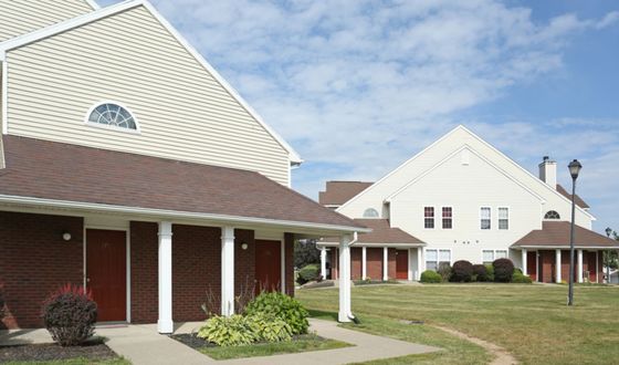 Charming residential community with classic architecture, featuring picturesque townhouses, red brick accents, and lush green lawns under a bright blue sky.
