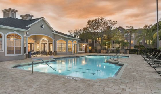 Luxurious apartment complex with a stunning sunset view over a sparkling pool, surrounded by stylish architecture and lush landscaping.