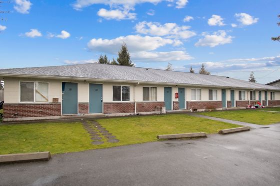 Charming row of brick-front apartments with blue doors, surrounded by a well-maintained green lawn under a vibrant blue sky.