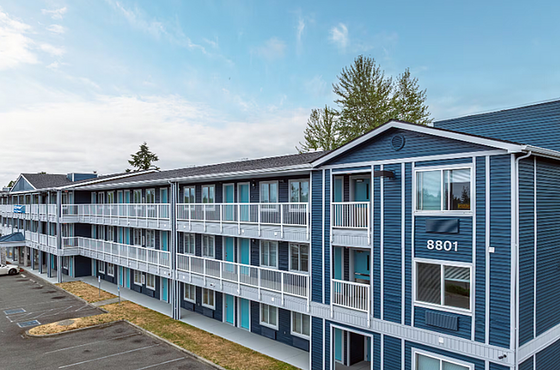 Charming three-story apartment building with spacious balconies and modern blue exterior, set against a serene sky.