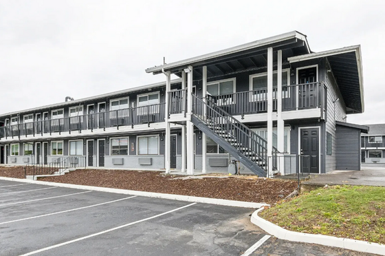 Contemporary apartment building with stylish gray facade, featuring private balconies and ample parking space.