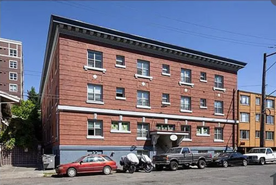 Charming brick apartment building with classic architectural details, ample parking, and a vibrant urban setting under a clear blue sky.