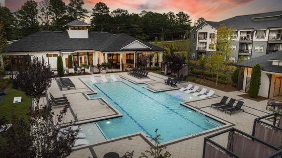 Luxe apartment complex with a resort-style swimming pool surrounded by elegant loungers and lush landscaping at sunset.