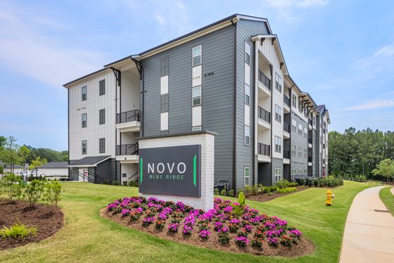 Elegant and modern apartment building at Novo Blue Ridge, surrounded by lush landscaping and vibrant flower beds, offering a serene residential atmosphere.