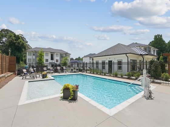 Inviting swimming pool area with modern lounge chairs, surrounded by charming residential buildings and lush greenery.
