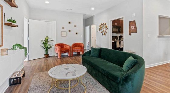 Bright and inviting living room with a plush green sofa, vibrant orange chairs, and modern decor, featuring stylish wood flooring and a cozy atmosphere.