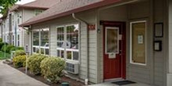 Charming apartment exterior with a welcoming red door, surrounded by lush greenery and modern siding.