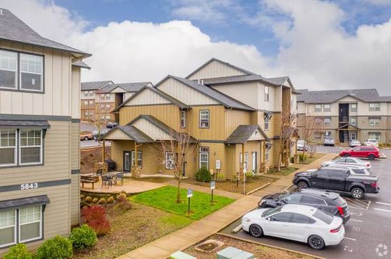 Charming residential apartment complex with modern architecture, ample parking, and well-maintained landscaping under a vibrant sky.